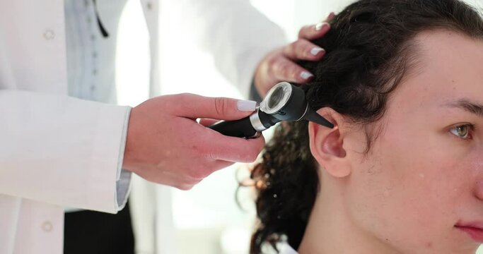 Female ENT doctor examines patient ear using otoscope
