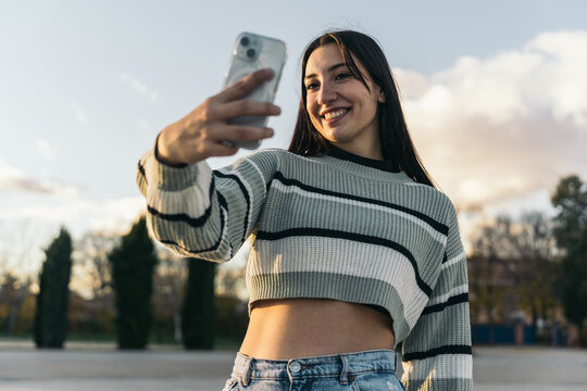 Smiling Young Caucasian Woman Taking a Selfie after Skating in an Urban Skate Park at Sunset. A joyful young girl capturing a selfie after a skate park session