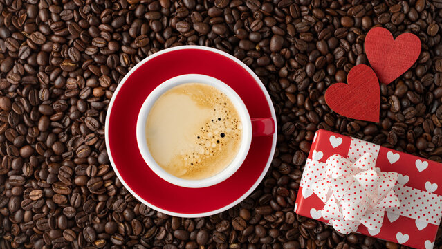 Romantic coffee beans background with red white cup of coffee, gift boxes and wooden hearts.