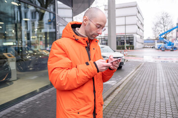 young 30-year-old man Outdoors uses smartphone on city street among modern buildings, European winter, Active Lifestyle, satellite communication, frosty weather