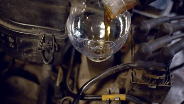 Refilling the crankcase with fresh engine oil after replacement. Close-up video footage from a car repair shop.