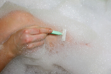 Fototapeta premium close-up woman shaving her legs in bath with foam. depilation
