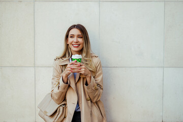Portrait of a happy stylish woman standing outdoors with coffee to go.