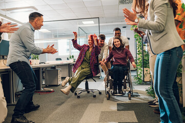Woman with disability and a hispanic woman racing together in the office at work