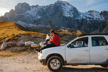 A young man sitting on the hood of his 4wd SUV car with his border collie dog on a break while...