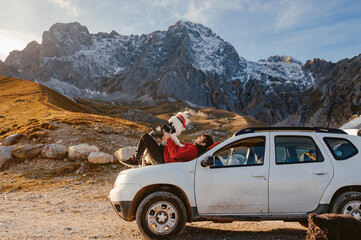 Man lying on the hood of his SUV car next to his faithful dog companion during an adventure trip in the mountains. traveling with dog.