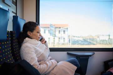 Young woman r talking on smart mobile phone while travelling by train. Female passenger riding a...