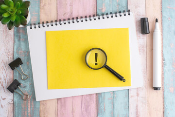 exclamation mark under a magnifying glass on a yellow background, top view, the mark is written in black marker