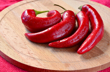 Chili peppers are red on the kitchen board on the table on a red background, water drops, copy space