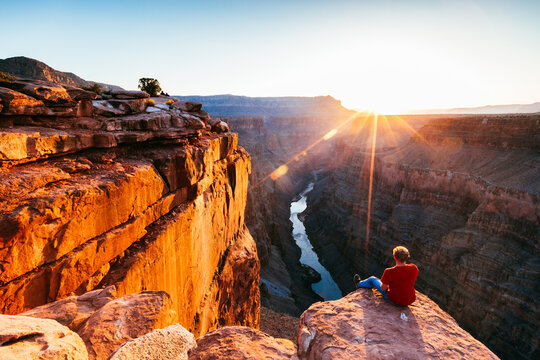 Man sitting on the edge of the Grand Canyon at sunrise, Arizona, United States