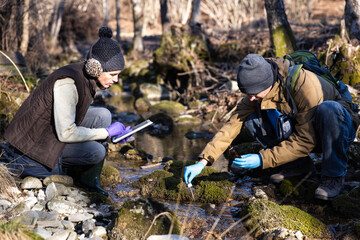 Caucasian Young Adult Biologists Collecting Water Samples from a Forest Water Stream in Winter