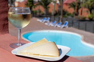 Spanish hard manchego, cow, sheep and goat cheese, cold white wine and blue swimming pool on background