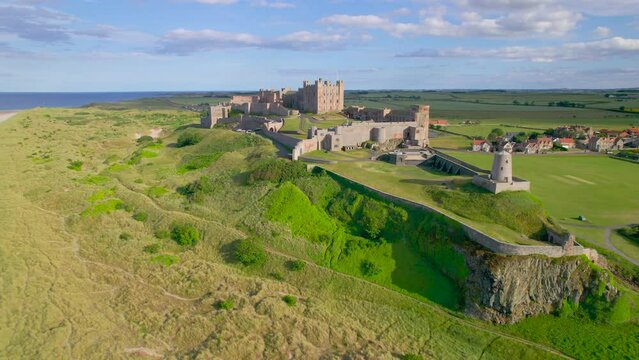 AERIAL: Beautiful view of historic Bamburgh Castle in an exceptional location. Stunning attraction with a remarkable fortress on top of a crag rising on the edge of green fields above a sandy beach.