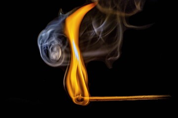 Burning match with smoke on a black background, close-up