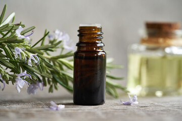 A dark bottle of aromatherapy essential oil with blooming rosemary plant