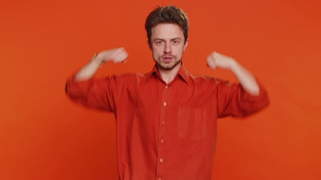 I am the best, choose me. Happy Caucasian man feeling very proud pointing himself, looking self-confident, overjoyed by success, making choice. Young guy isolated on studio orange background indoors