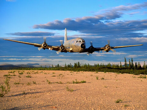 A DC-6 aircraft lifts off the remote Salmon-Trout airstrip in NE Alaska with midnight sun lighting the way.
