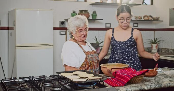 The granddaughter happily hugs her grandmother while they cook tortillas.