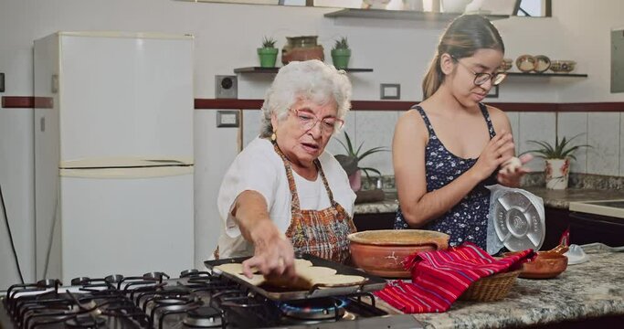 Grandmother and granddaughter make artisanal tortillas in their home kitchen.