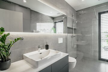 The image depicts a sleek, modern bathroom. It features a white sink, large mirror, glass shower...