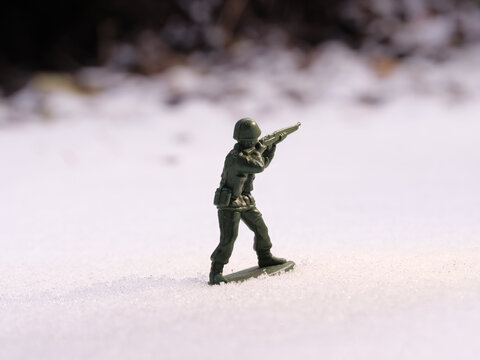 War toy soldier in bright daylight on a cold, snowy battlefield landscape. Frozen earth mounds, trees in the blurred dark background.