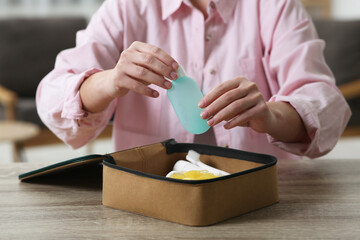 Woman packing cosmetic travel kit into compact toiletry bag at wooden table indoors, closeup. Bath accessories