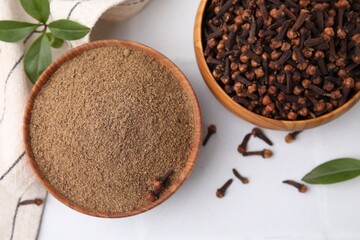 Aromatic clove powder and dried buds in bowls on white table, flat lay