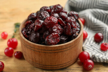 Tasty dried cranberries in bowl and fresh ones on wooden table, closeup