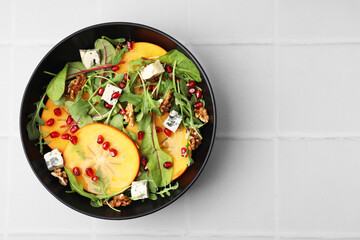 Tasty salad with persimmon, blue cheese, pomegranate and walnuts served on white tiled table, top view. Space for text