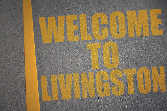 asphalt road with text welcome to Livingston near yellow line.