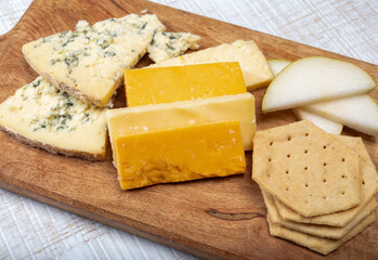 English cheeses collection, mature and coloured cheddar cheese and semi-soft, crumbly old stilton blue cheese close up