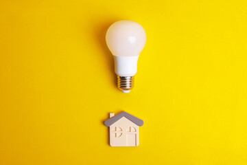 White light bulb and a house symbol on yellow background. Concept saving energy with LED lamp at...