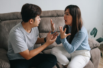 Asian young couple sitting at sofa having quarrel and arguing to each other. Domestic problems...