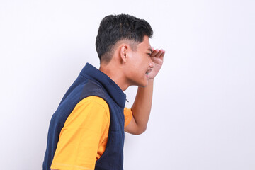 Side view of Asian man wearing vest, standing over white background and looking far away with hand over head.