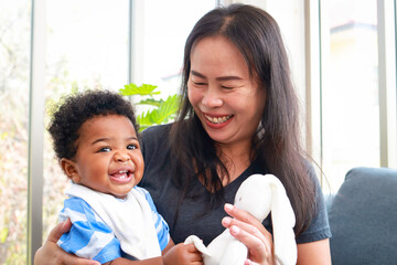 An Asian woman takes care of a little black boy. She hugs him and smiles happily. Raising children....