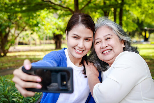 Asian family concept. Caring for the elderly to be happy. An elderly mother and her daughter take pictures playing in an outdoor park. They smile happily.