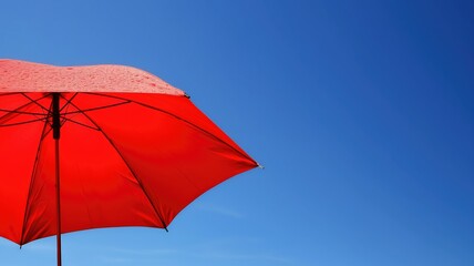 Bright red umbrella with water droplets against a clear blue sky