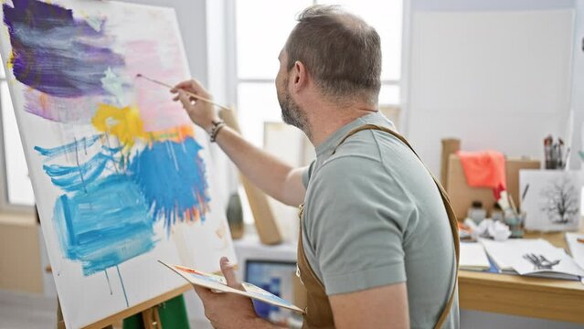 Handsome mature man painting on canvas in a bright art studio, portraying creativity and concentration.