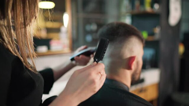 Young female barber making men's undercut haircut hairstyle using Haircut Clipper in Modern style barber shop. Haircare service local small business, cosmetics and personal care industry 4K video