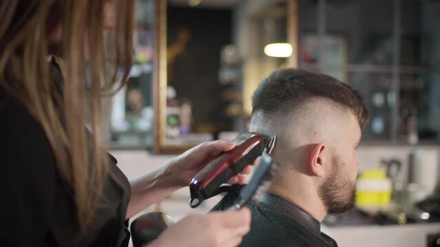 Young female barber making men's undercut haircut hairstyle using Haircut Clipper in Modern style barber shop. Haircare service local small business, cosmetics and personal care industry 4K video