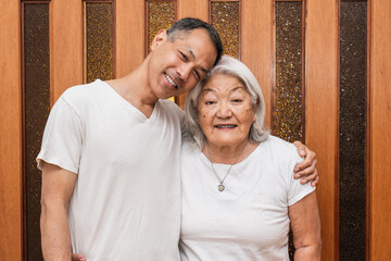 Asian mother and adult son smile and look at camera. Mother's day