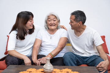 Adult children, with smiles on their faces, embrace their joyful elderly mother as she sits on a sofa.