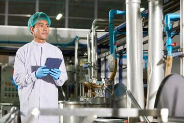 worker working on tablet beside large industrial pot in the beverage factory
