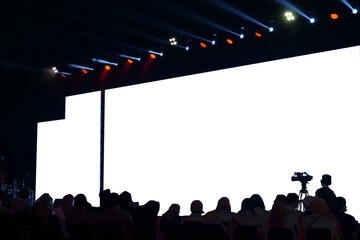 Audience in silhouette watching a presentation with a large blank projection screen, event and conference concept.