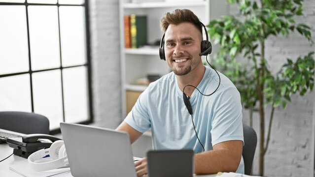 Smiling man wearing headset working on laptop in modern office interior