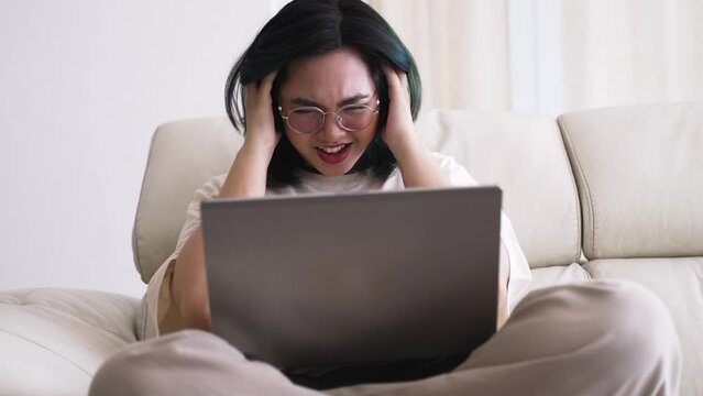 with glasses touching head and Asian woman closing eyes resting while sitting cross legged near laptop