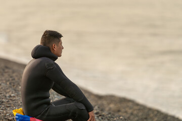Fisherman in wetsuit sitting gazing the ocean