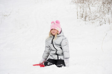 Fototapeta na wymiar A girl in a snowy forest rides an ice slide down a slide. Photo of a child in a winter forest. Winter, winter holidays, vacations, vacations.