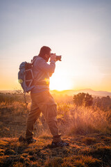  With camera and backpack, the photographer chases the golden light that caresses the mountains at dawn.adventurer concept, local travel, - obrazy, fototapety, plakaty