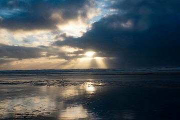Obraz premium Coastal seascape on beach with dramatic sun rays shining through dark clouds